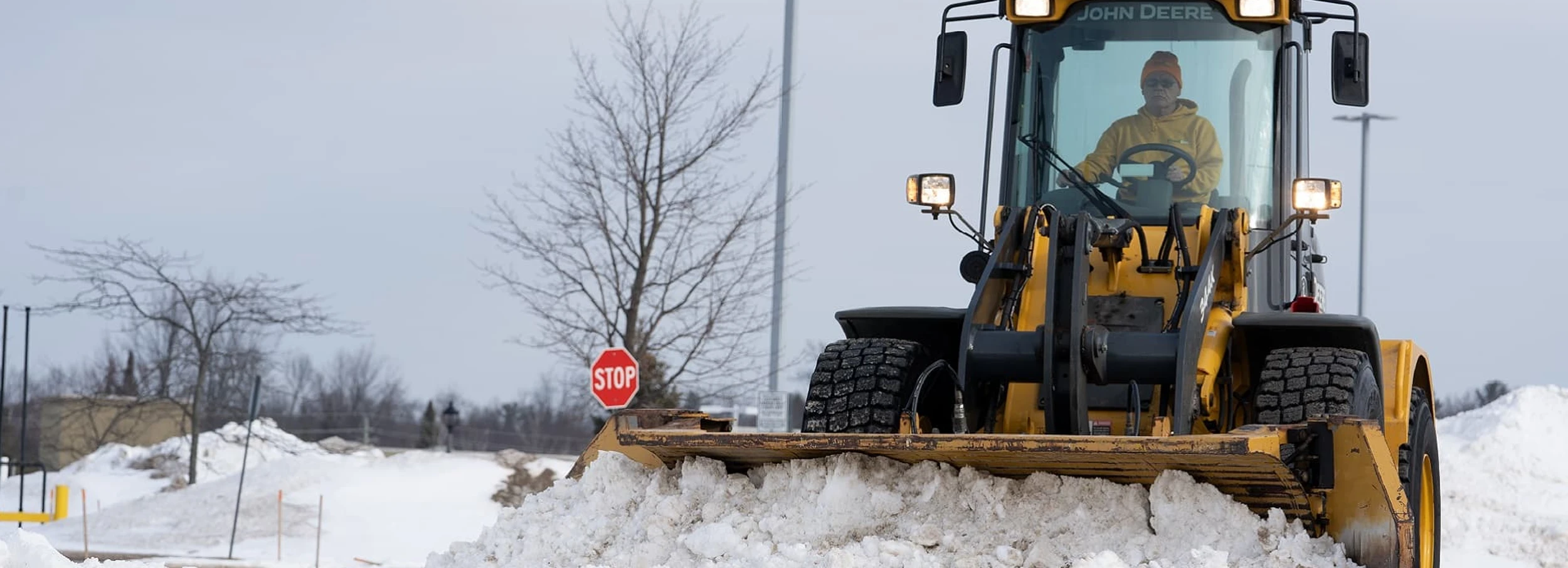 Grounds Guys employee in yellow sweatshirt and winter hat driving snowplow.